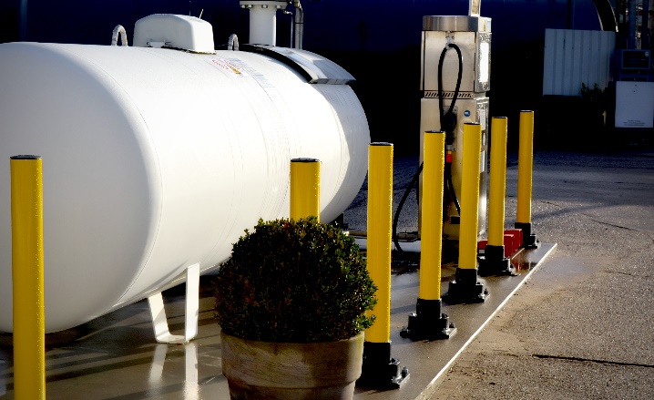 Yellow SlowStop rebounding bollards protect white gas tank and gas pump from accidental vehicle damage.